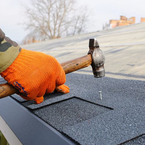 contractor-hand-with-glove-and-hammer-installing-asphalt-shingles-roof-close-up-longview-tx